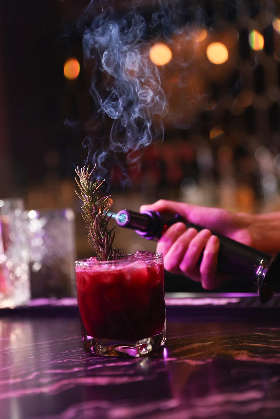 A bartender torching a garnish over a red cocktail