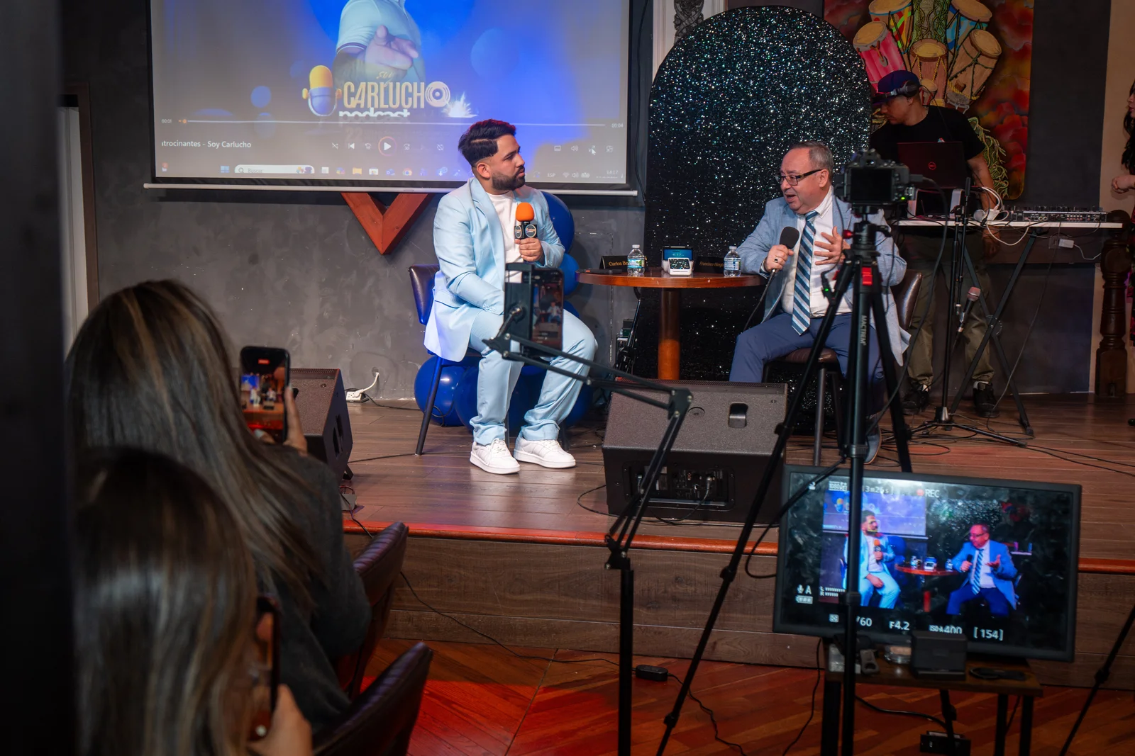 A live interview on stage, with a camera and monitor in the foreground